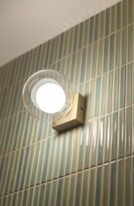 Detalle de pared revestida con piezas cerámicas pequeñas en formato vertical y distintos tonos verdes, realzada por iluminación integrada en el Proyecto Mallorca.