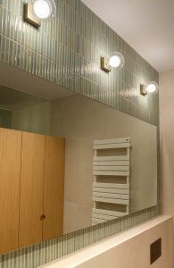 Detalle de pared revestida con piezas cerámicas pequeñas en formato vertical y distintos tonos verdes, realzada por iluminación integrada en el Proyecto Mallorca.