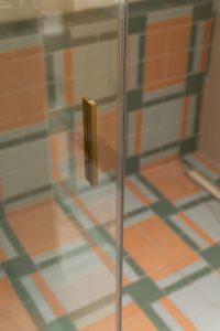 Detalle de la ducha con suelo y lateral revestidos con la misma cerámica en combinación de piezas en tonos gris, verde y terracota del Proyecto Mallorca.